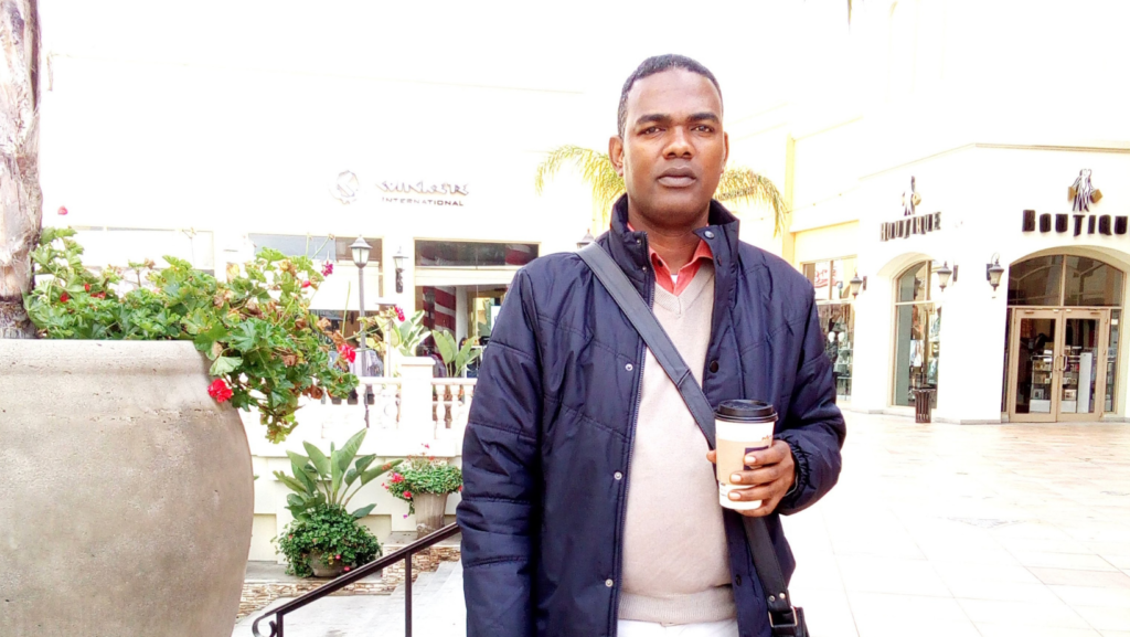 Calvin Murray standing outdoors at a shopping center in Mexico, wearing a dark jacket and holding a coffee cup, with a confident expression.